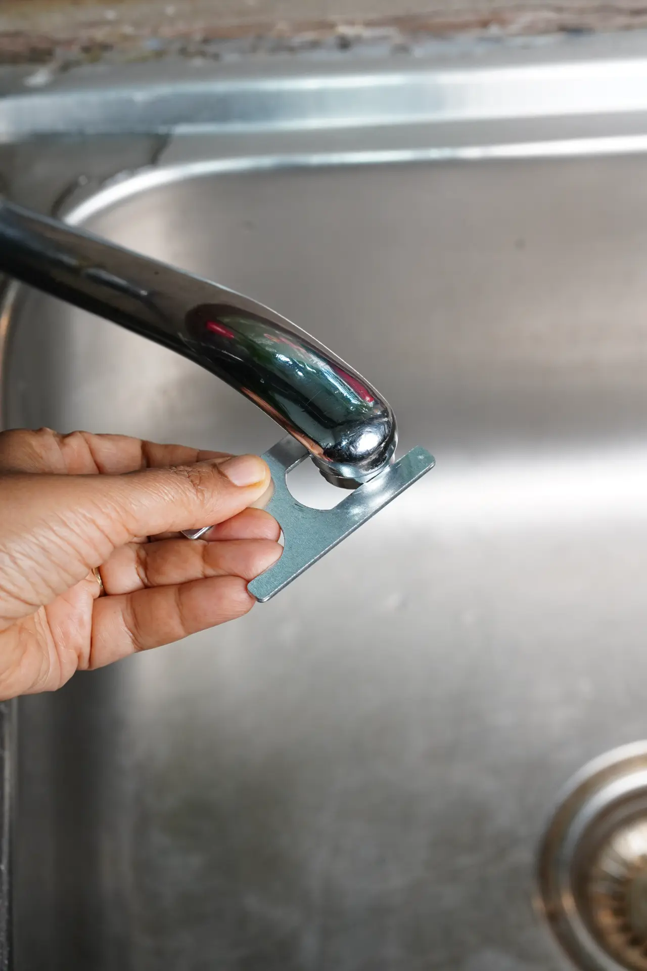 Hand holding the Kitchen by Verra metal tap adapter against a chrome kitchen faucet